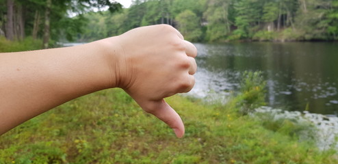 right Human hand thumbs down in nature next to a river