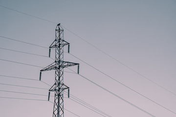 Posts with wires of high voltage on background of sky in sunlight. Monochrome backdrop image of many wires in sky with copy space. Power lines in faded tones.