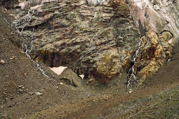 Detailed natural texture of giant rock of fantastic shape covered with snow and ice in highlands. Small waterfalls and brooks flow down mountainside. Fantasy mountain landscape of majestic nature.