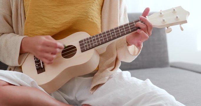 Woman practice ukulele and sitting on sofa at home