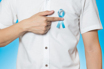 Men's healthcare concept - close up of male hand pointing to light blue ribbon for prostate cancer...
