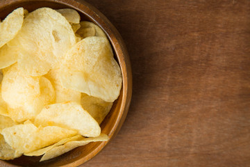 Top view of potato chips in wooden bowl on wooden background.