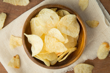 Top view of potato chips in wooden bowl putting on linen and wooden background.