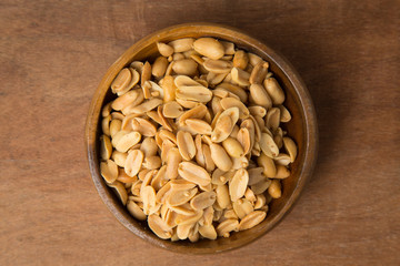 Roasted peanuts in wooden bowl on wooden background.