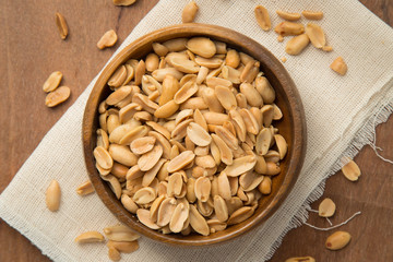 Roasted peanuts in wooden bowl putting on linen and wooden background.