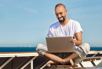 A man using his laptop at sea in a yacht.