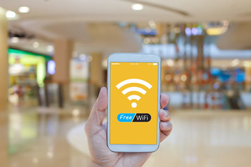 Hand holding smartphone with Free WiFi on screen over blurred in shopping mall background