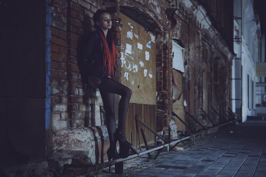 A sexy girl stands under a lantern and poses in the image of a seductive prostitute. The concept of selling love.. Woman in a dark with a cigar, it looking sad eyes down.