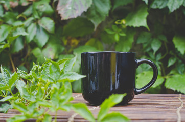 A single solo blank black coffee mug on the wooden table in the backyard. 