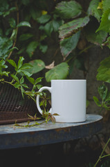 A long view of a blank white coffee mug on the overgrown table edge of the cafe