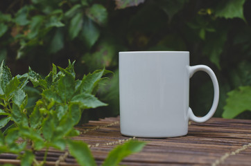 A single solo blank white coffee mug on the wooden backyard cafe table in the morning. 