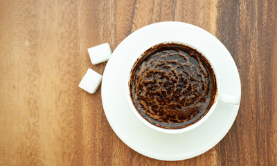 White cup with coffee, two slices of sugar, brown background.