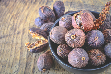 Black cardamom pods with open shell in ceramic bowl and Indian spice on wooden background.