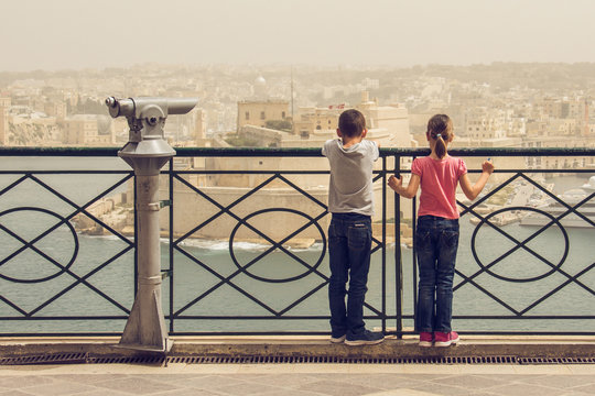 A Boy And A Girl Enjoy View From Sightseeing Point. Children On Holidays. Two Children Look At Fort Saint Angelo From Upper Barrakka Garden(Malta).