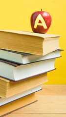 Back to school and knowledge concept. Stack of books and fresh red apple with mark A on wooden background and trendy yellow wall