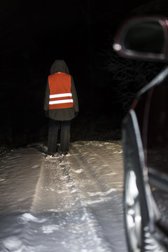 Woman standing on a snowy road in the dark in Finland. Car headlights illuminate the person. She is wearing a reflective vest.
