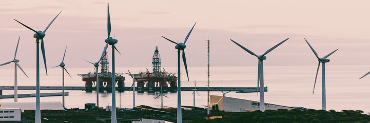 Group of windmills and solar panels for electric power production and oil rigs on coast.