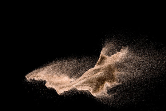 Dry river sand explosion. Golden colored sand splash agianst dark background.