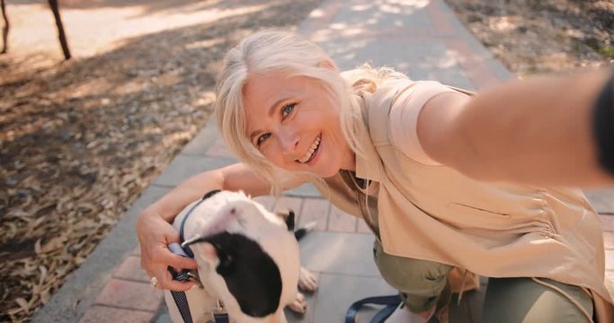 Happy fashionable senior woman taking selfies with dog in nature