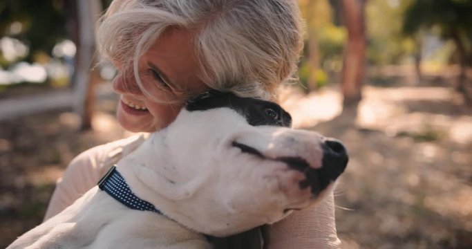 Smiling senior woman hugging pet dog in park in autumn
