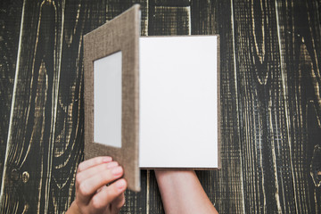 Top view photography of new brown modern photo book with empty frame for photo and plastic pages. White woman opens album with love. Isolated on wooden background. Horizontal color picture. - Powered by Adobe