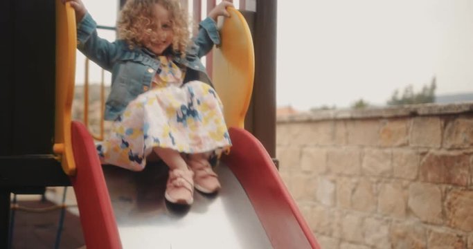 Happy little girl playing and having fun on playground slide