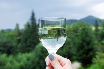 a glass of wine with an inverted image in the girl's hand, against the backdrop of mountains and coniferous forests