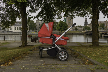 Obraz na płótnie Canvas red baby stroller stands alone in a park by the river