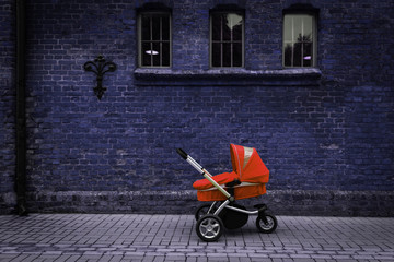 red stroller stands on the road near the wall