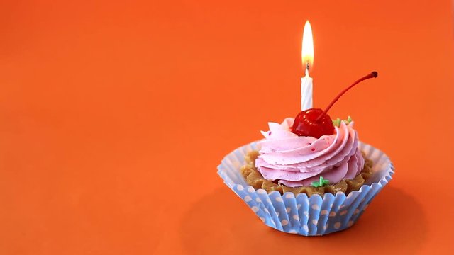 Birthday cake with cherry, pink cream and burning candle for birthday on orange background