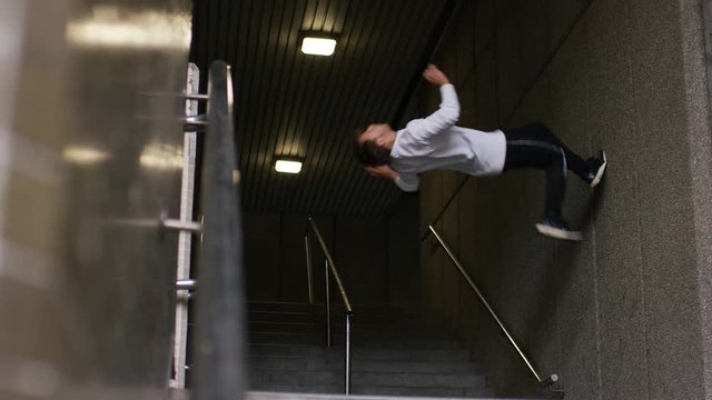 Parkour athlete runs up a wall before flipping backwards and jumping off screen, in slow motion