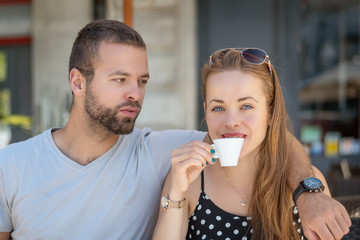 Summer in the city. Happy young couple sitting on a terrace. Girl with a cup of coffee.