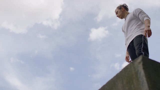Young man doing parkour stops at the edge of a building before leaping off, in slow motion 
