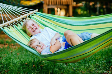 Two happy blond scandinavian children swinging and relaxing in garden hammock together.