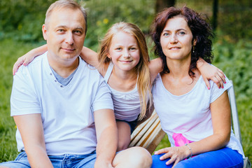 Portrait of joyful family with child. Father, mother and daughter having fun outdoors in garden, playing together in summer park.