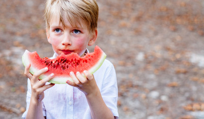 Blond hair school boy with blue eyes eat watermelon outdoor in autumn day.