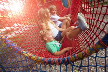 Group of three blond scandinavian children siblings having fun in red net tunnel in playground or...