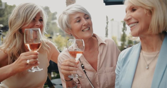 Fashionable senior friends relaxing together and drinking wine on patio