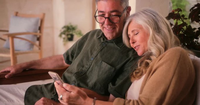 Happy mature couple using smartphone and relaxing together at home