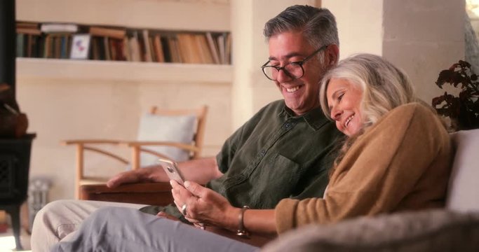 Loving senior couple using smartphone and laughing together at home