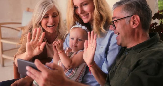 Smiling three-generation family relaxing at home and video-calling on smartphone