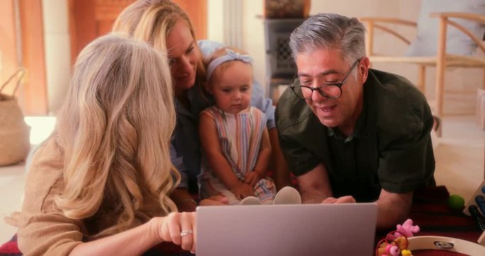 Happy three-generation family with little granddaughter watching cartoons on laptop