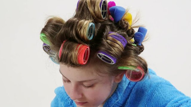 Teenage girl with hair curlers painting nails after bath.