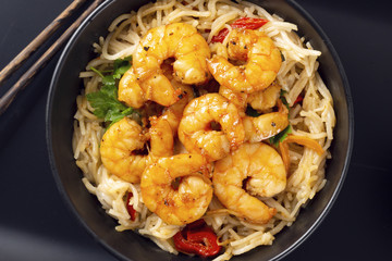 Fried prawns and rice noodles with spices on a black plate. Black background. Eastern food. Copy space. Horizontal shot.