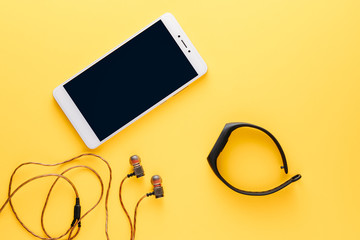 fitness concept with mobile phone, earphones and fitness tracker on yellow background