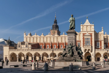 Obraz premium The Adam Mickiewicz statue and the Cloth Hall in the historic center of Krakow, Poland on a beautiful sunny day