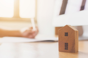 Wooden home model on wood table with hand signing the document contract loan or mortgage property investment