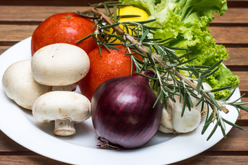Fresh vegetables, mushrooms, tomatoes and onion in a white plate