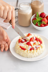 women's hands cut with a knife cake. Delicate strawberry cheesecake with coconut. Delicious homemade cake with Fresh berries on light table.
