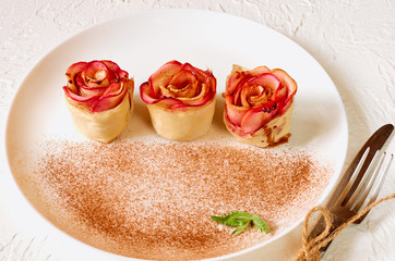 Mini rose tarts with apples and mint leaves on the white plate. Side view